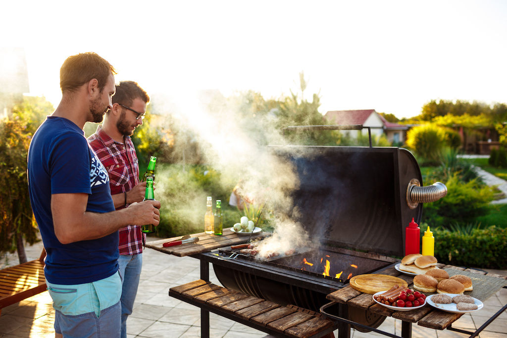 Two guys barbecuing meat and vegetables on a grill